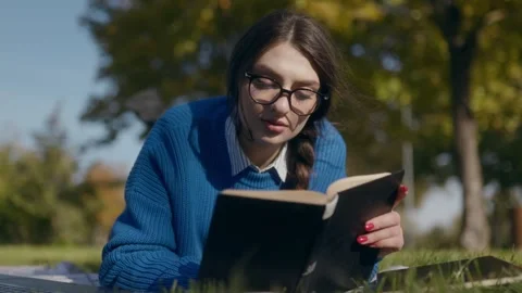 Young student reading a book on the grass in a park Stock Footage 300265385