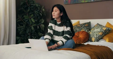 A young student sits on a bed in a room with a laptop and studies for exams. The Stock Footage 229348649