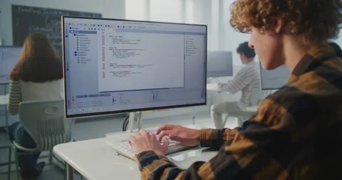 Young Student Sits at Desk, Focused on Computer Screen While Typing Programming Stock Footage 318526138