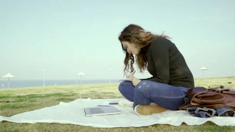 Young student sits on the ground in a park by the sea on a sunny day 動画素材 148504753
