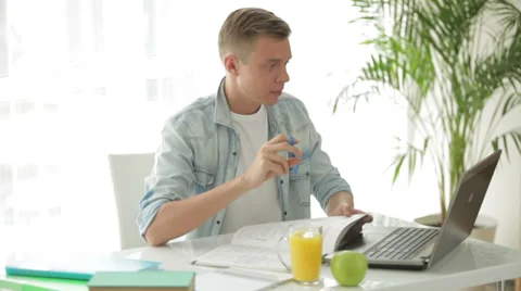 Young student sitting at table using laptop and writing in notebook Video stock 27691927