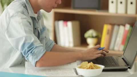 Young student sitting at table using laptop and eating chips Stock Footage 27691932