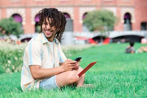 Young student smiling and using smartphone and laptop computer at the park Stock Photos