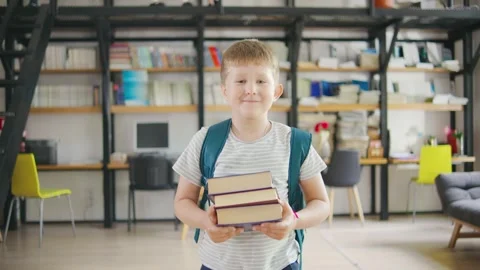 A young student, with a smiling face, is carrying a stack of books in a bright Video stock 284275486