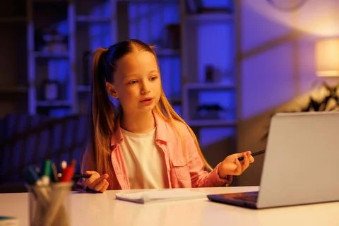 A young student studies remotely at home in the evening using a laptop. The Stock Photos