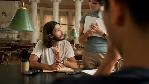 Young student studying with tutor in library. University students sitting Stock Photos