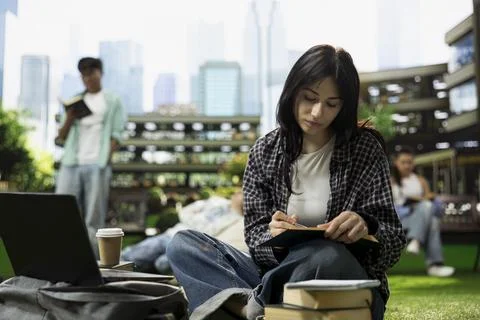 Young student taking notes beside laptop with open book and coffee Stock Photos