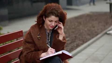 Young student talking on cellphone and writing notes in the park Stock Footage 74304431