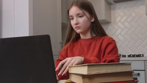 Young student typing on laptop with stack of books Видео 311780099