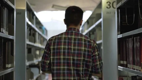Young student walking between book shelf and searches for his book in library Stockbeeldmateriaal 80554662