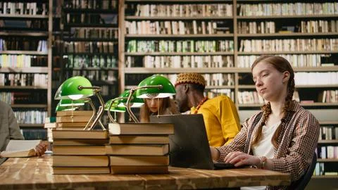Young student working on laptop taking notes at library table with open book Stock Photos
