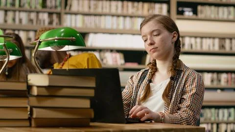 Young student working on laptop taking notes at library table with open book Stock Photos