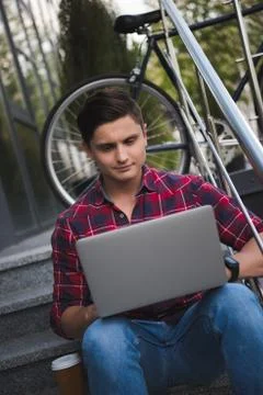 Young student working on laptop while sitting on stairs at the street Photos