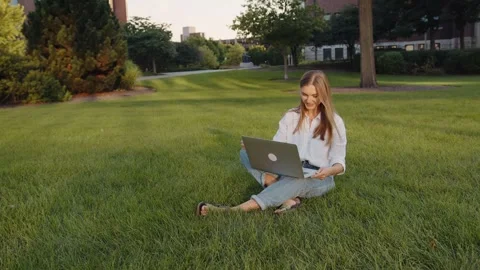 A young student working while sitting on the grass with a laptop. 스톡 동영상 320076218