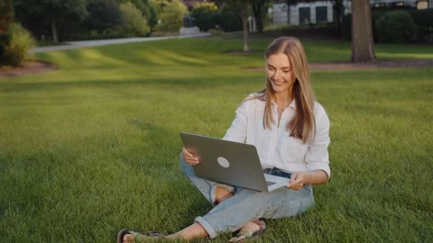 A young student working while sitting on the grass with a laptop. Video stock 321622525