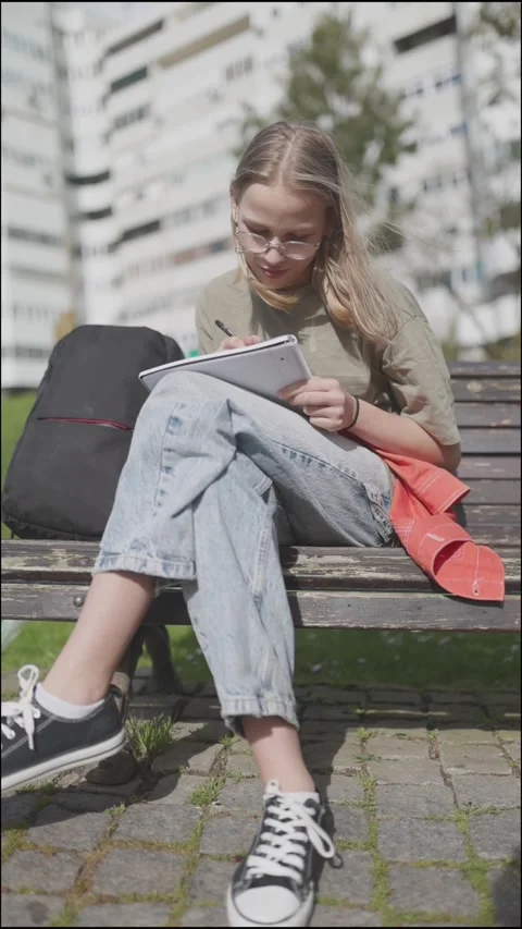 Young student writing outdoors on a bench Stock Footage 314066035