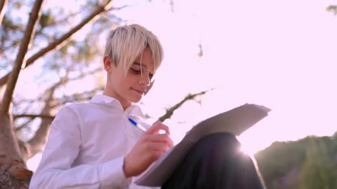 Young student writing outdoors under a tree Stock Footage 316957694