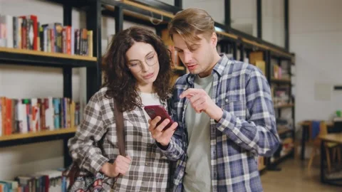 Young students couple engaged in conversation while looking at a smartphone in a Stock Footage 318093341