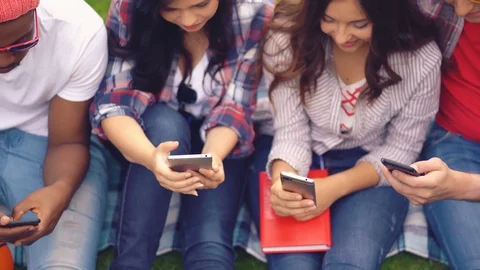 Young students of different races sit picking smartphones Stock Footage 126284970