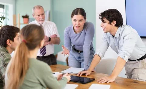 Young students discussing a topic around table monitored by senior teacher 스톡 사진