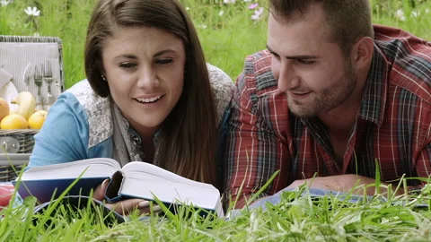 Young students/ happy couple learning or reading  with a book in the park, while Stock-Footage 199632317