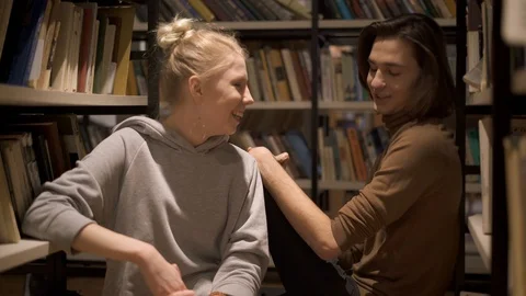 Young students sitting and talking between bookshelves 動画素材 105597086