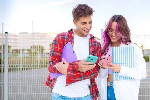 Young students smiling and using smartphones with colorful notebooks outdoors Stock Photos