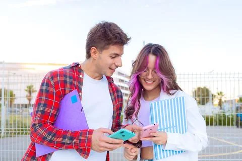 Young students smiling and using smartphones with colorful notebooks outdoors Stock-Fotos