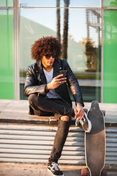 Young stylish black man using smart phone in sunny city Stock Photos