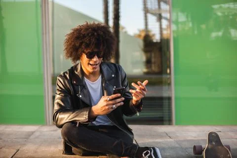 Young stylish black man using smart phone in sunny city Stock Photos