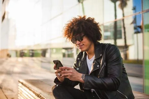Young stylish black man using smart phone in sunny city Stock Photos