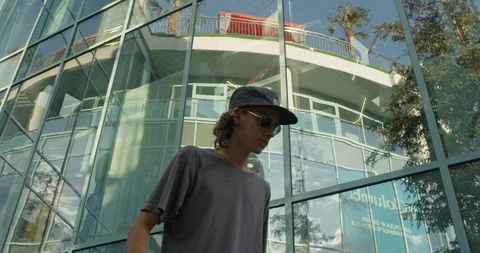 Young stylish curly guy skating on a skateboard near a glass building. Slow Stock Footage 90129287