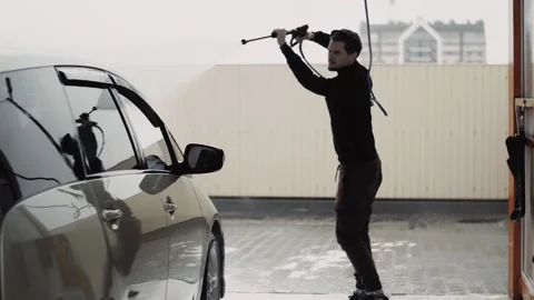 Young stylish curly guy uses a high pressure jet water to clean a car Stock Footage 144676216
