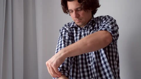 Young stylish curly man gets dressed and bends the sleeves of his shirt at home. Stock Footage 312391522