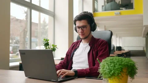 Young stylish customer support service worker removes headphones, looking at Stock Footage 217733578