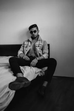 Young stylish guy in denim jacket on the bed. black and white photo with fine Stock Photos