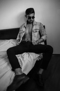 Young stylish guy in denim jacket on the bed. black and white photo with fine Stock Photos
