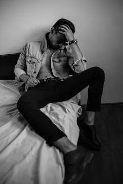 Young stylish guy in denim jacket on the bed. black and white photo with fine Stock Photos