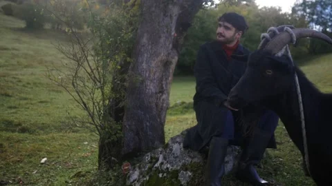 A young stylish guy walks with a goat near his house in forest Stock-Footage 194084286