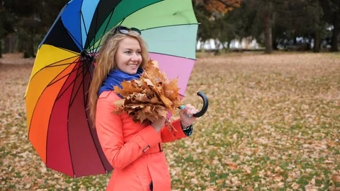 A young stylish long-haired blonde girl with large colored umbrella in red coat Stock Footage 106353232
