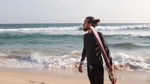 A young stylish man with a beard is standing on the beach with a surfboard Stock Footage 108024648