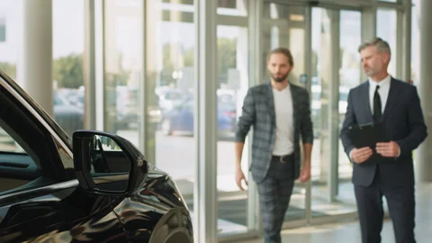 Young successful customer man deciding to buy new auto in showroom. Happy car Stock Footage 240499378