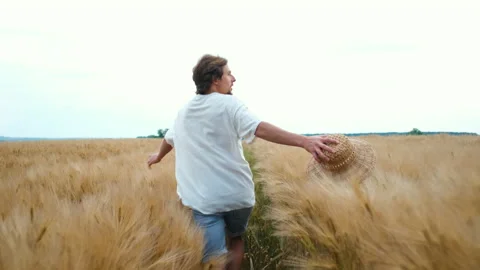 A young successful farmer in light clothes and a hat runs happily across the Stock Footage 134050085