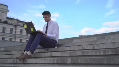 Young successful guy student working on the street on laptop. A man in a white Stock Footage 91419266