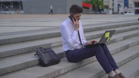 Young successful guy student working on the street on laptop. A man in a white Video stock 91419492