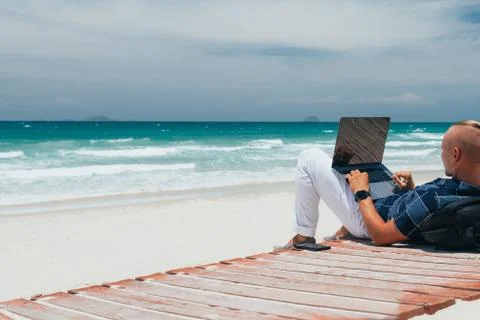 Young successful guy working using a laptop, sitting on the seashore Stock Photos