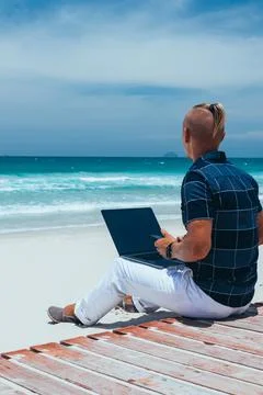Young successful guy working using a laptop, sitting on the seashore Stock Photos