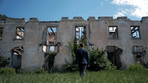 Young successful man in a jacket goes to an abandoned ruined house Stock Footage 128744521