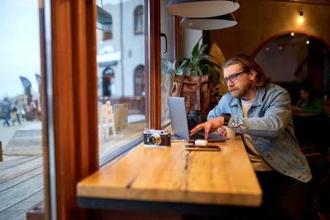 Young successful man sitting at cafe and surfing internet on laptop. freelance Stock Photos