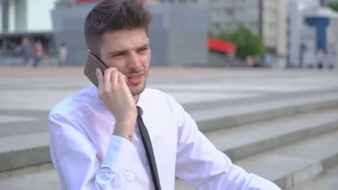 A young successful man is sitting on the steps and talking on the phone. White Stock Footage 91494688